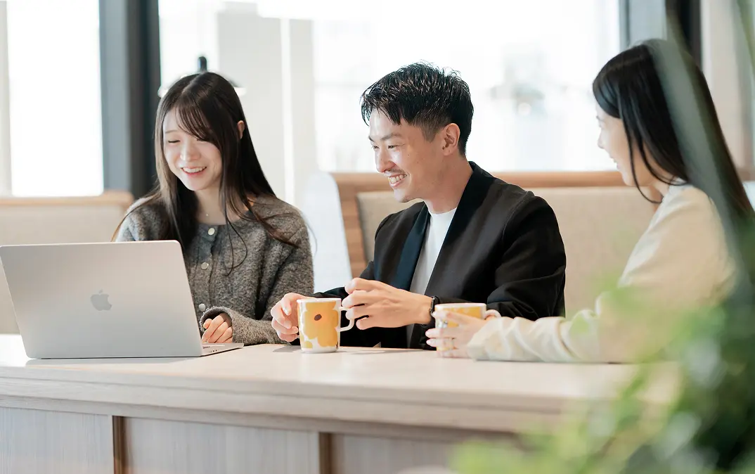 カウンター席でノートパソコンを囲み、笑顔で会話をしながら打ち合わせをするマナリンクの社員３人