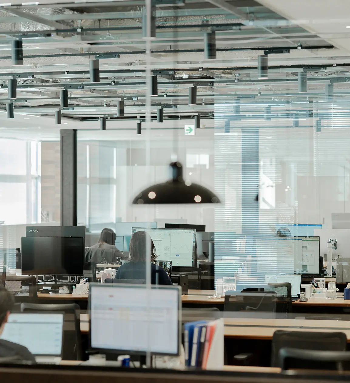 ガラス張りのオフィスで、パソコン作業をするマナリンクの社員がいる開放的なワークスペース